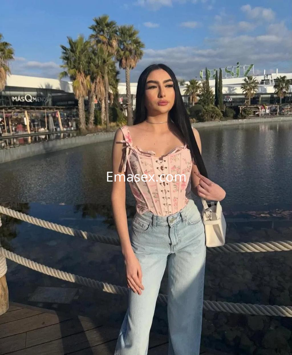 Escort en Zaragoza con cabello largo y lacio, viste un top rosa y jeans claros, posando junto a un lago.
