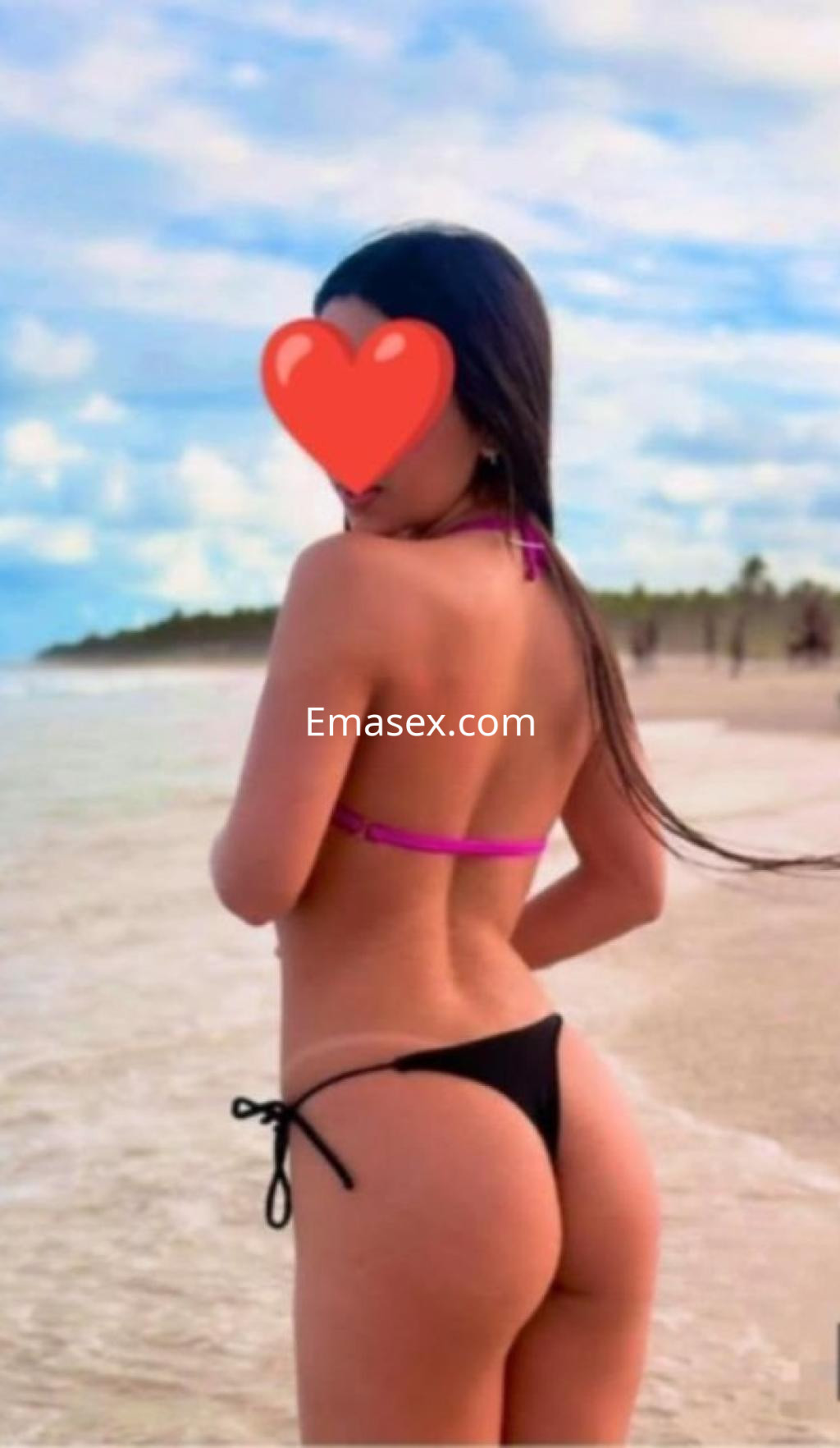 Puta de espaldas en la playa, con un bikini negro y tirantes rosas, disfrutando del paisaje de Ibiza.