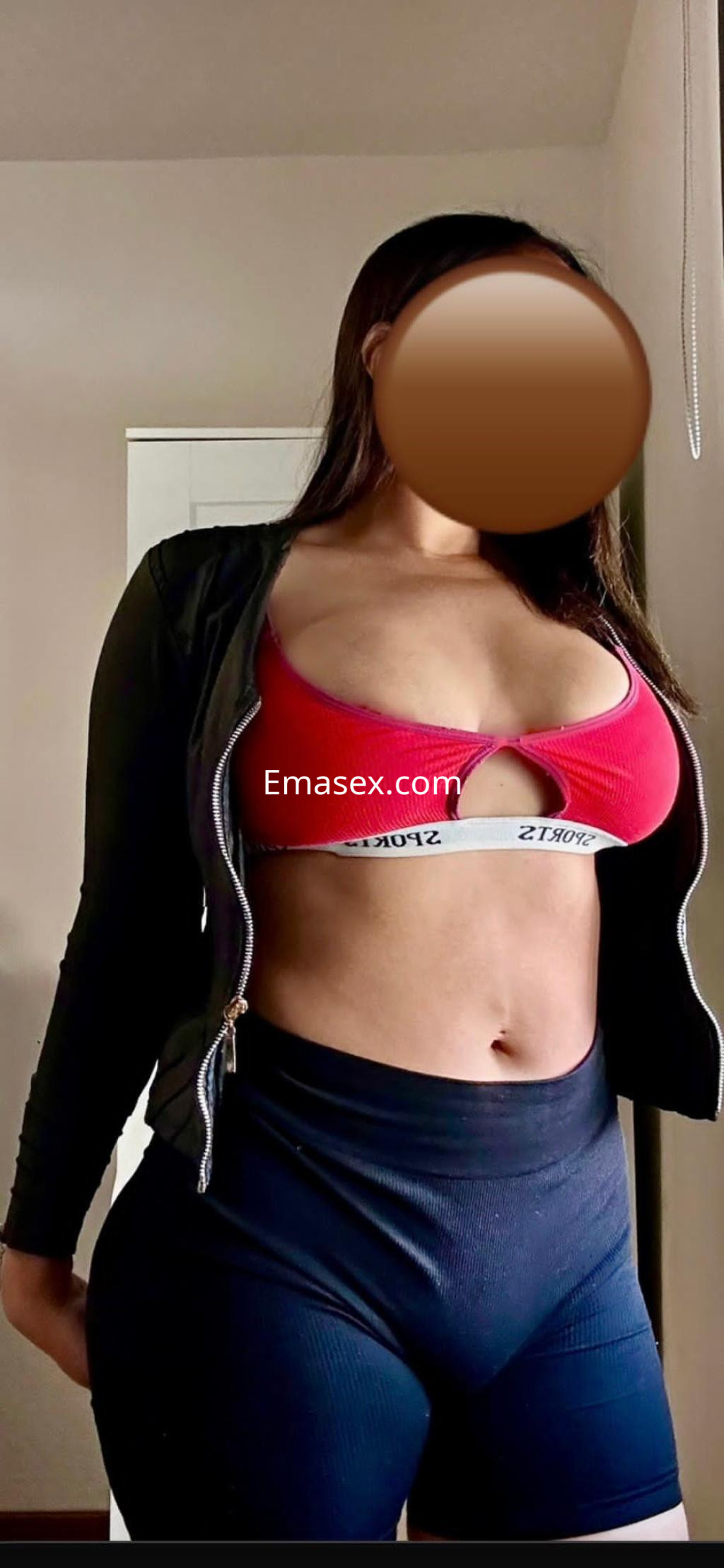Escort en Santiago viste un top rojo y pantalones cortos oscuros, posando con una mano en la cadera.