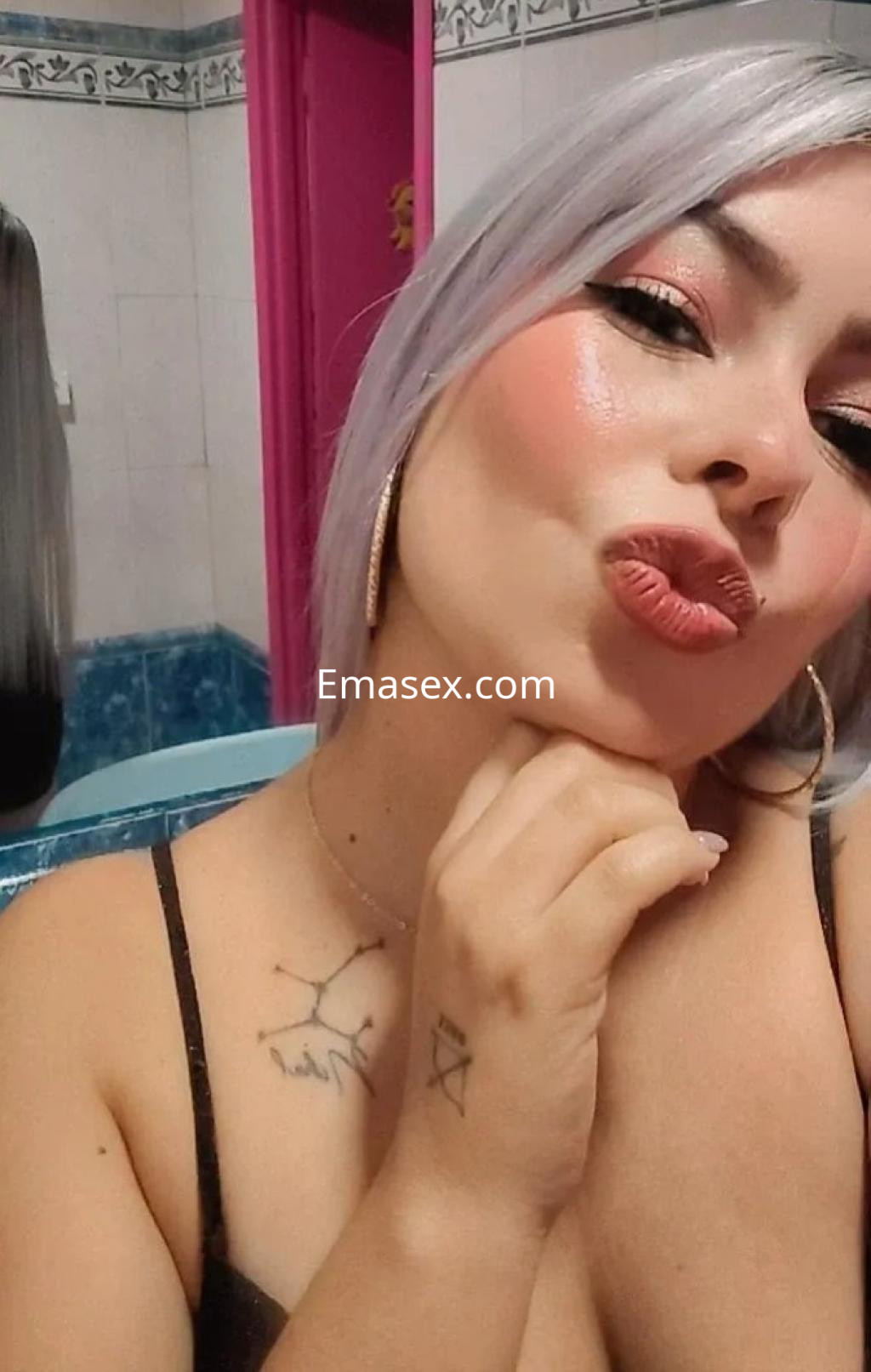 Escort en Córdoba, con cabello corto y plateado, viste una blusa negra y posa de forma coqueta.