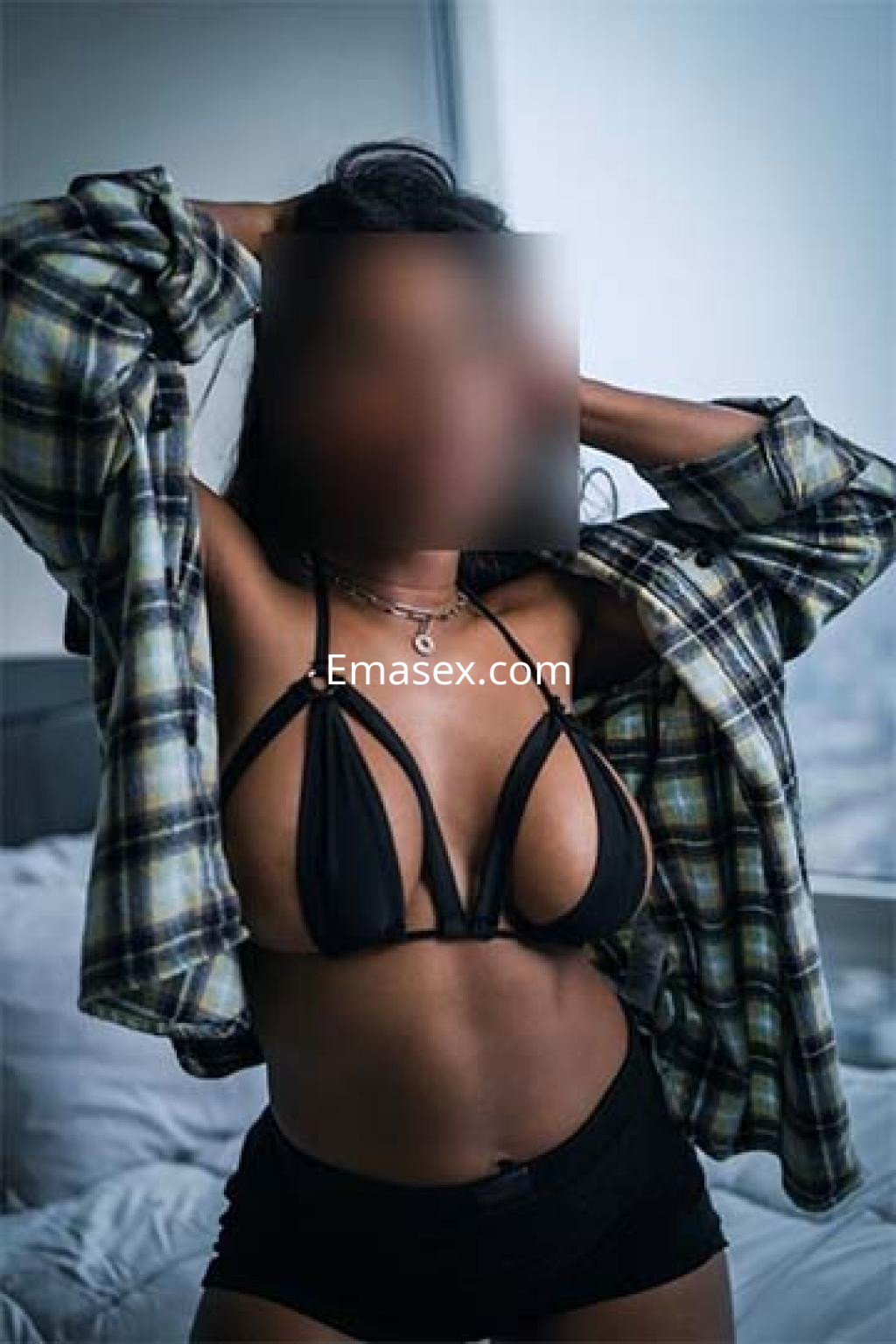Escort en Logroño posando con un sujetador negro y una camisa de cuadros, mostrando una actitud segura.