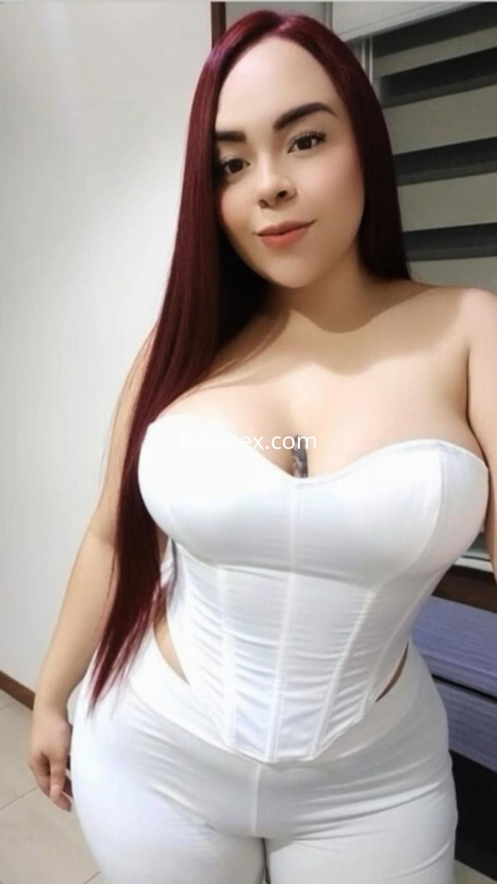 Escort en Córdoba con cabello largo y lacio de color rojo, vistiendo un corset blanco y pantalones ajustados.