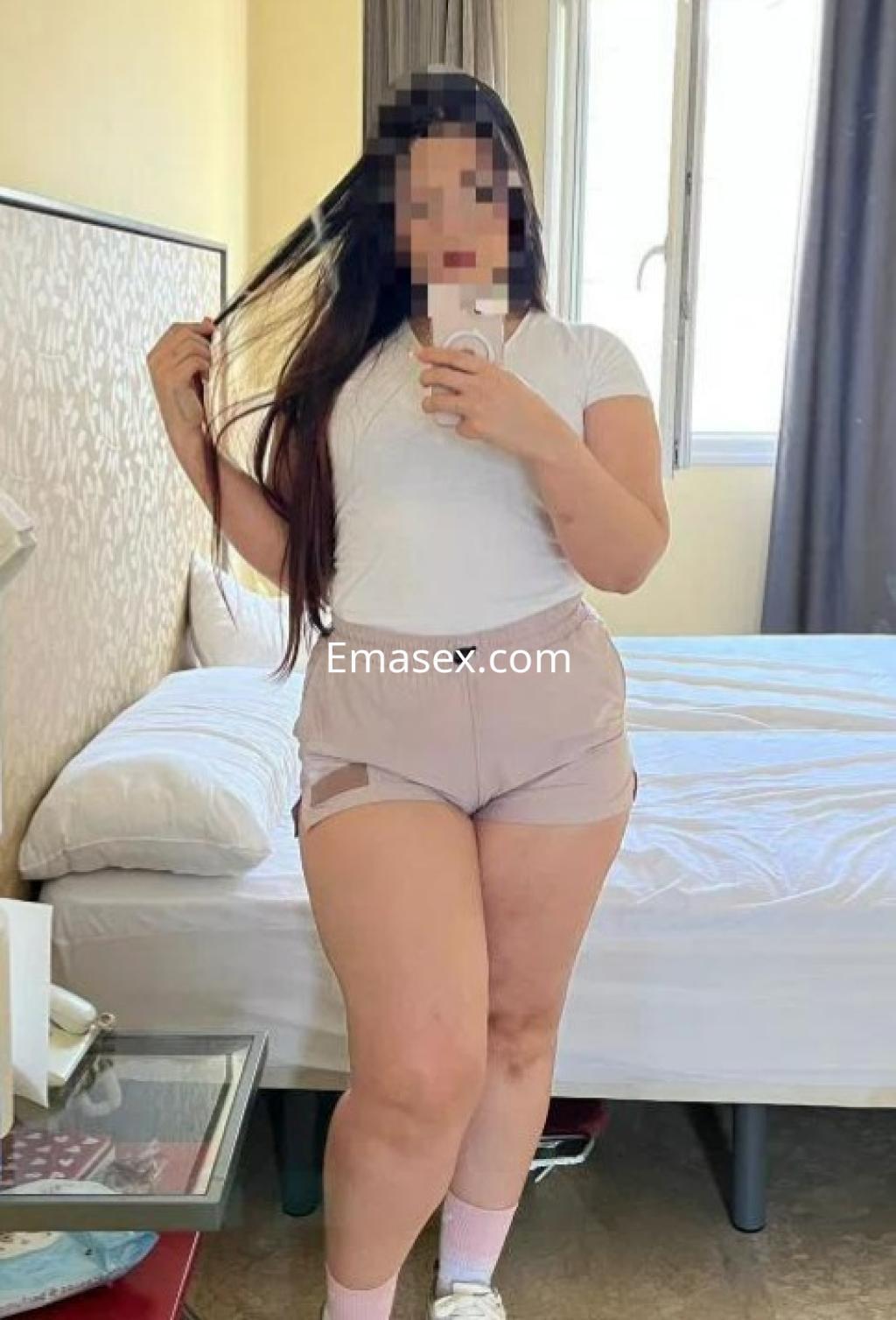 Escort en Zaragoza posando con una camiseta blanca y pantalones cortos, mientras sostiene su cabello largo.