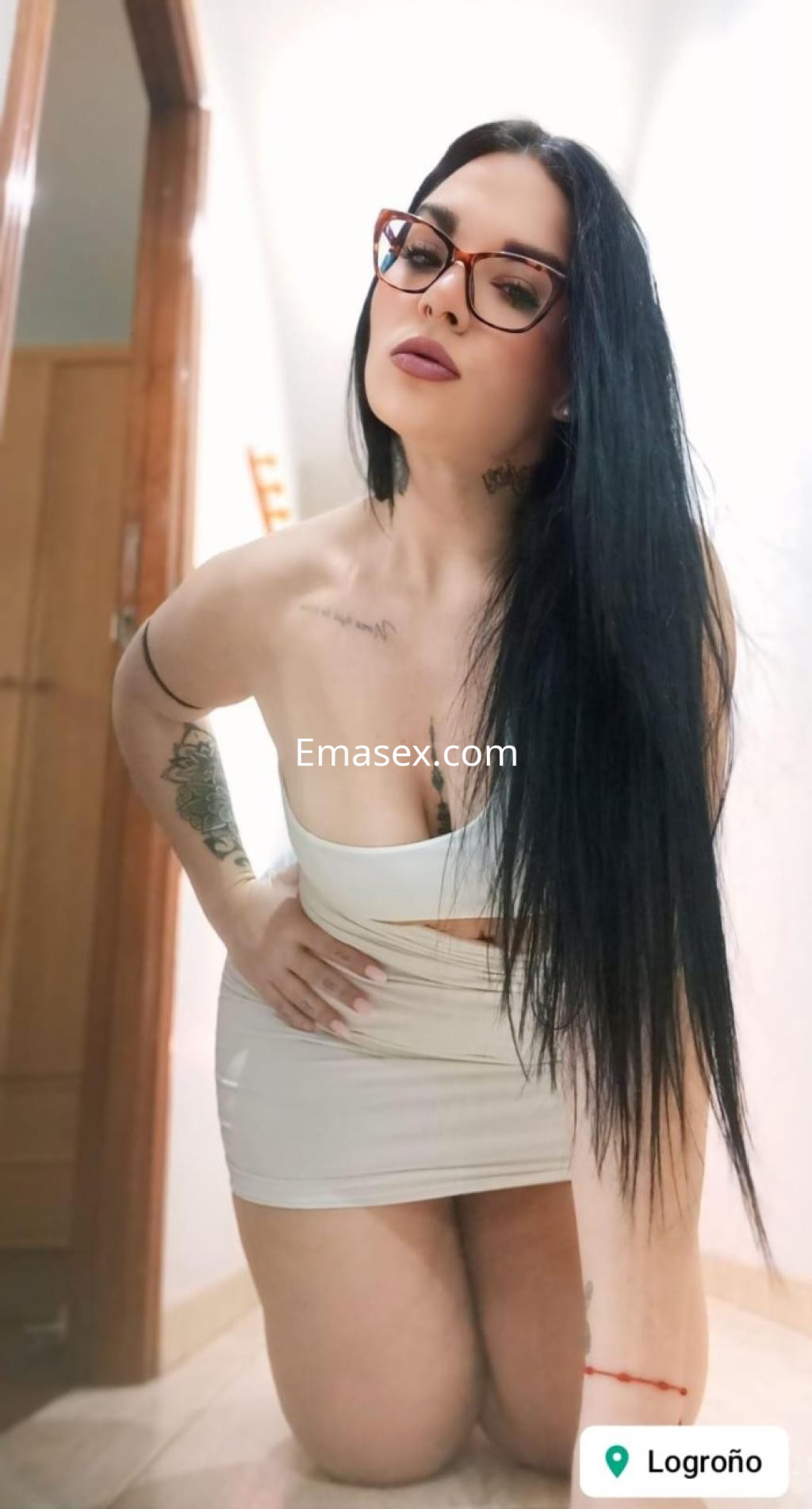 Escort en Pontevedra, con cabello largo y lacio, viste un vestido ajustado y gafas, posando en un ambiente interior.