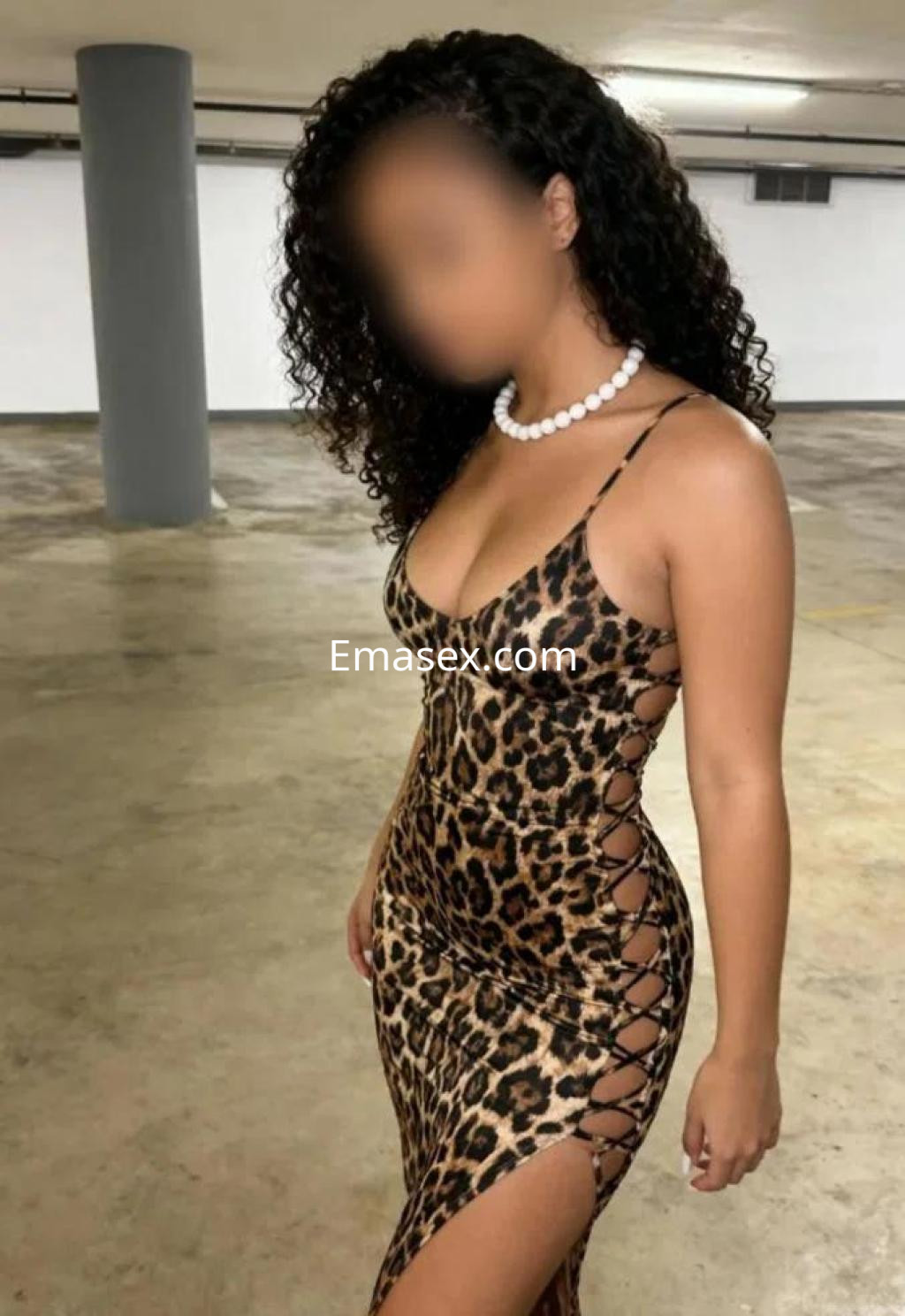 Escort en Barcelona luciendo un vestido de leopardo con tirantes finos, en un fondo de garaje.