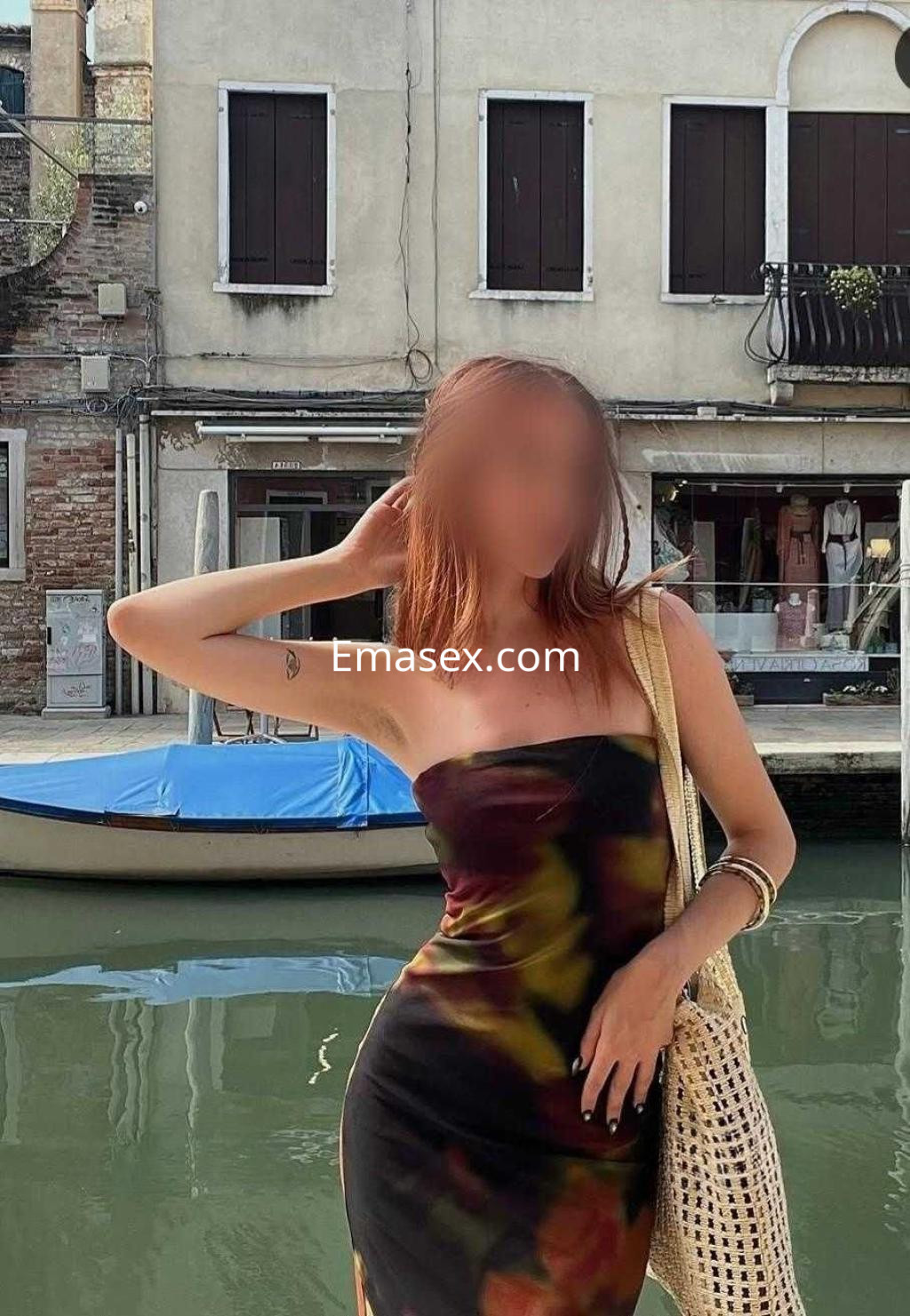 Escort en Barcelona, luciendo un vestido ajustado de colores oscuros, posando frente a un canal y un barco.