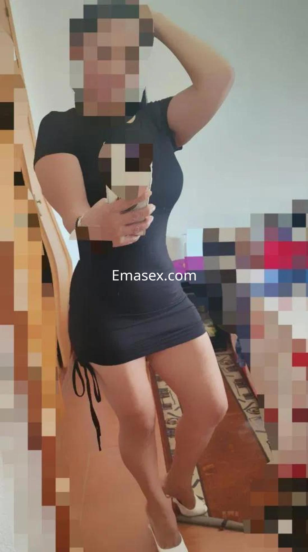 Puta en Cádiz, posando con un vestido negro ajustado que resalta su figura y sandalias blancas.