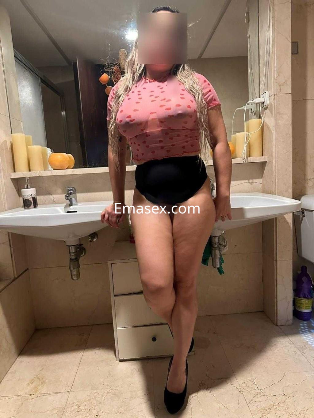 Escort en Madrid con blusa rosa con estampado y short negro, posando en un baño elegante.
