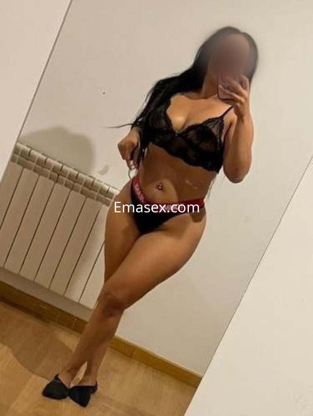 La puta en Ourense posa frente al espejo con lencería negra y una actitud seductora.