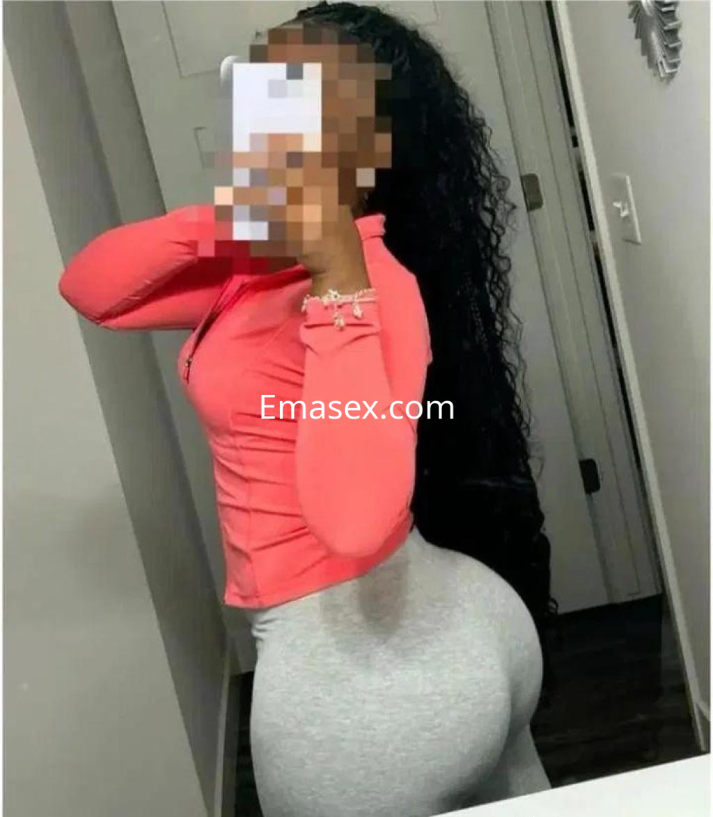 La puta en Salamanca posa de perfil con un ajustado conjunto de sudadera rosa y leggins gris, mostrando su figura.