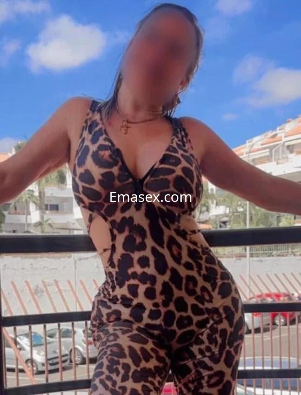 Escort en Tenerife luciendo un traje de leopardo ajustado, posando en un balcón con fondo urbano.