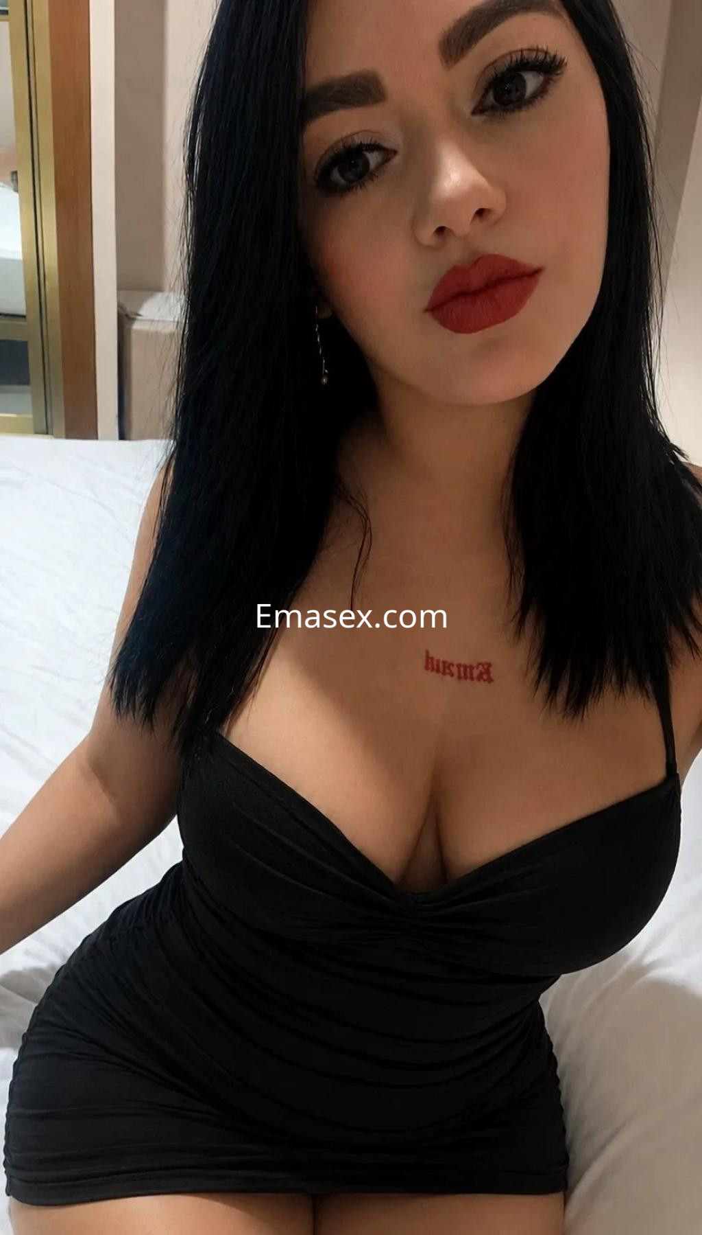 Puta en Valencia posando con un vestido negro ajustado, cabello oscuro y labios rojos, en un entorno interior.