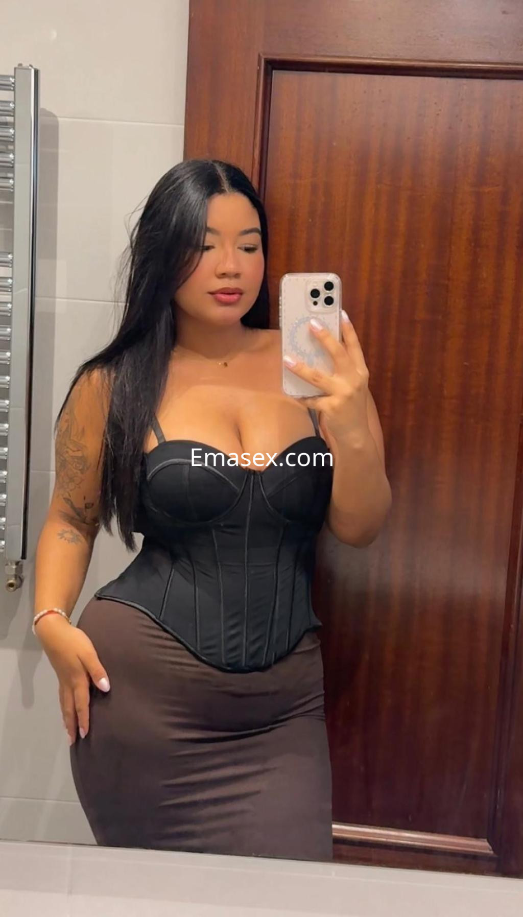 Escort en Pamplona con cabello largo y oscuro, luciendo un corsé negro y una falda ajustada en un espejo.