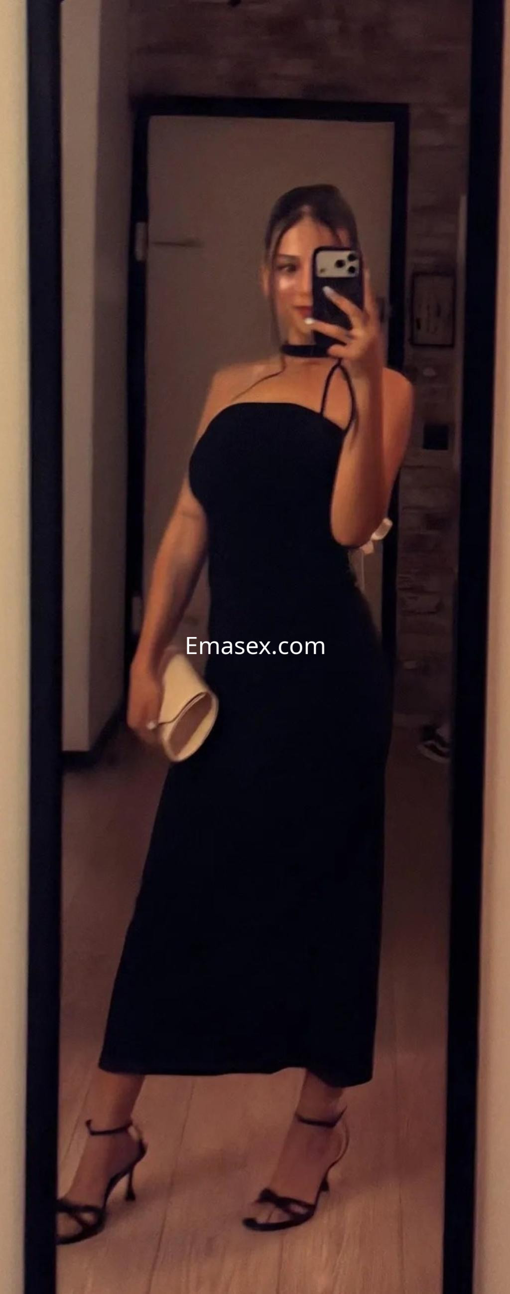 La puta posa frente al espejo en Palma de Mallorca, luciendo un vestido negro ajustado y tacones altos.