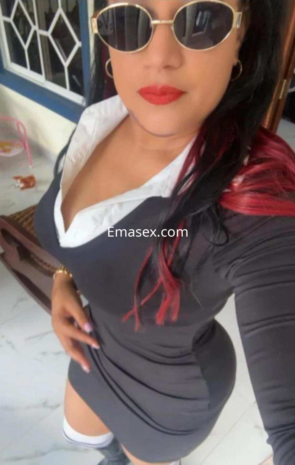 Escort en Coruña con vestido negro ajustado, cuello blanco, gafas de sol y cabello largo con puntas rojas.
