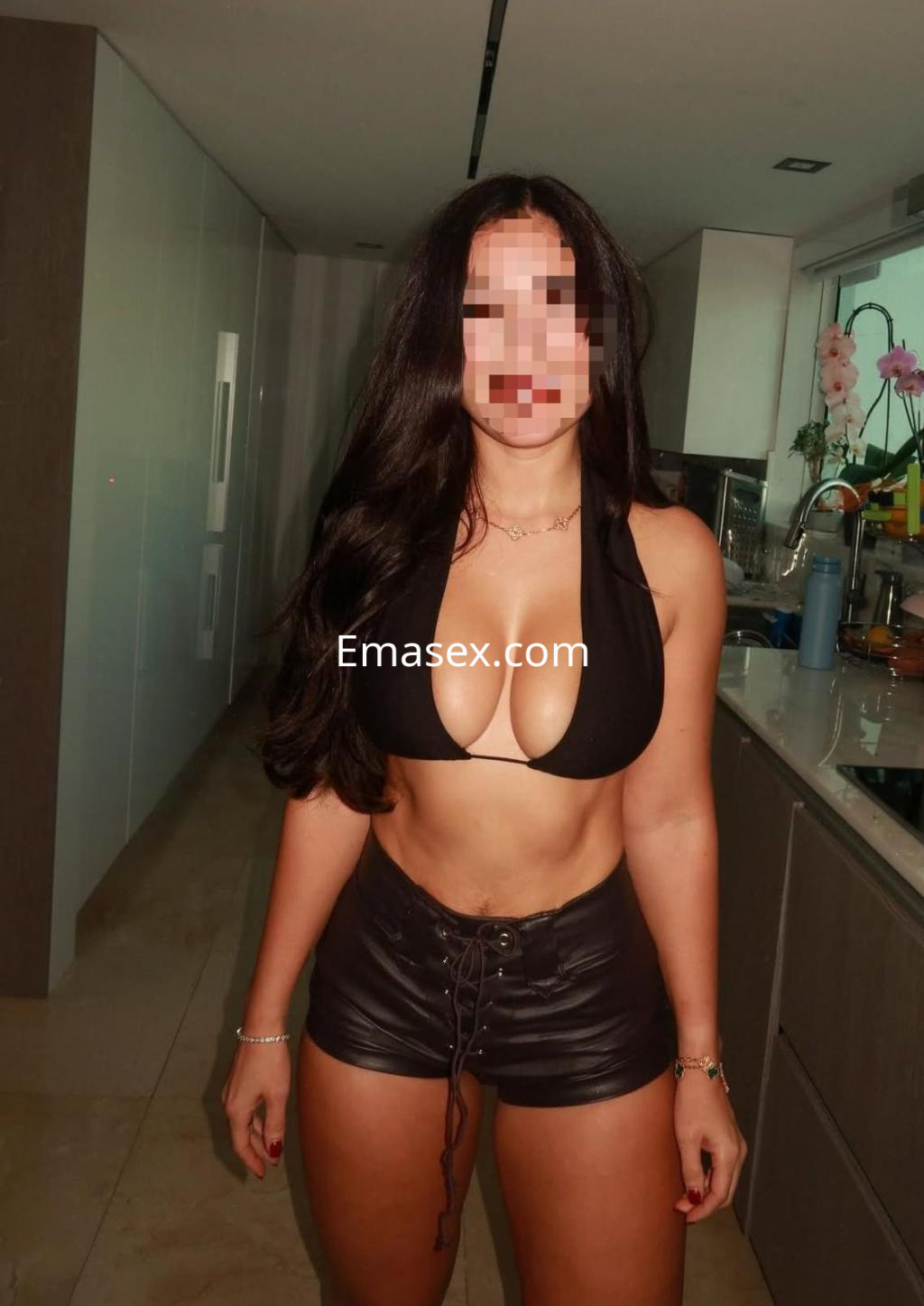 Escort en Pamplona con bikini negro y shorts de cuero, posando en una cocina moderna y luminosa.