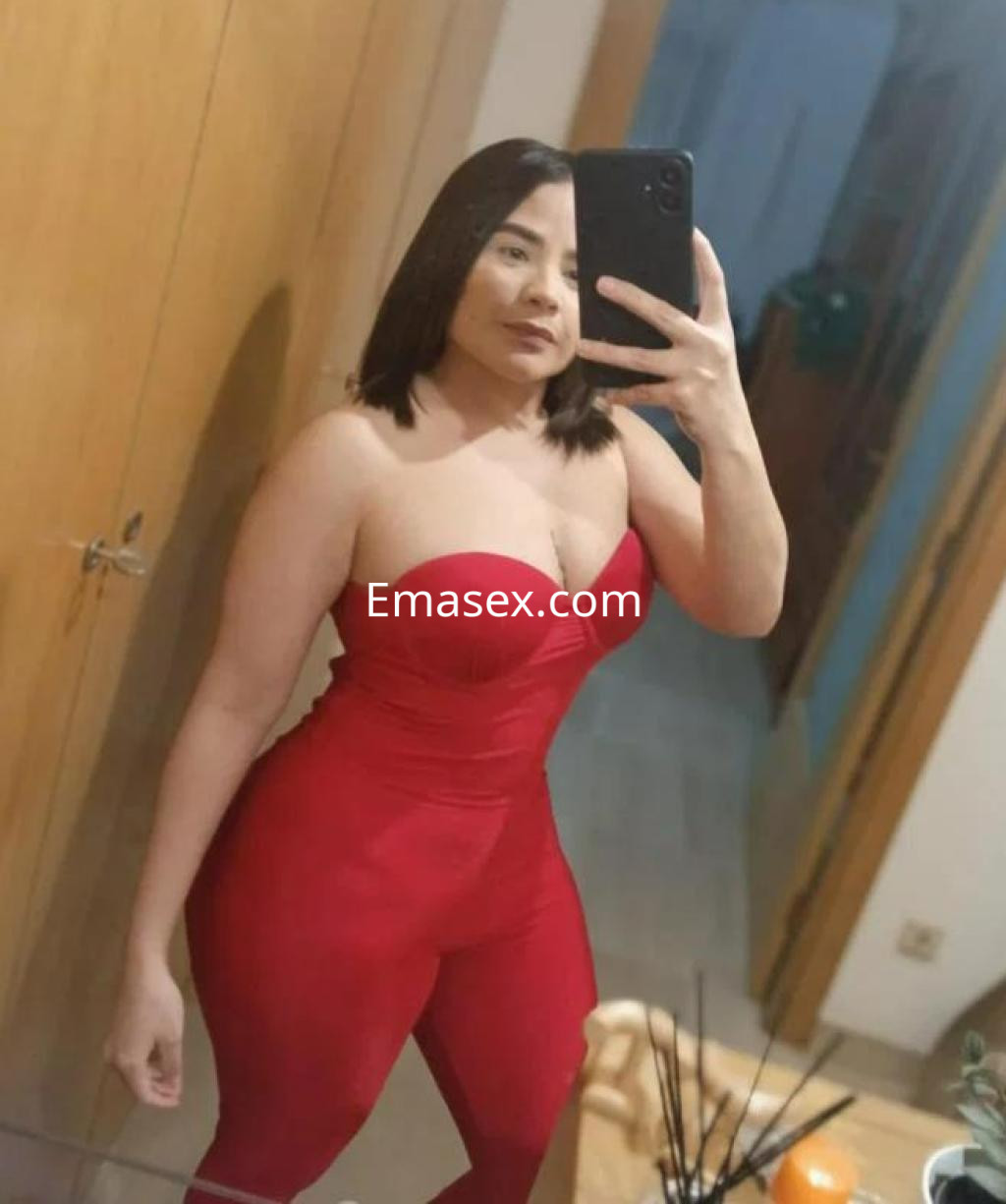 Escort en Barcelona, posando frente al espejo con un ajustado mono rojo que resalta su figura.