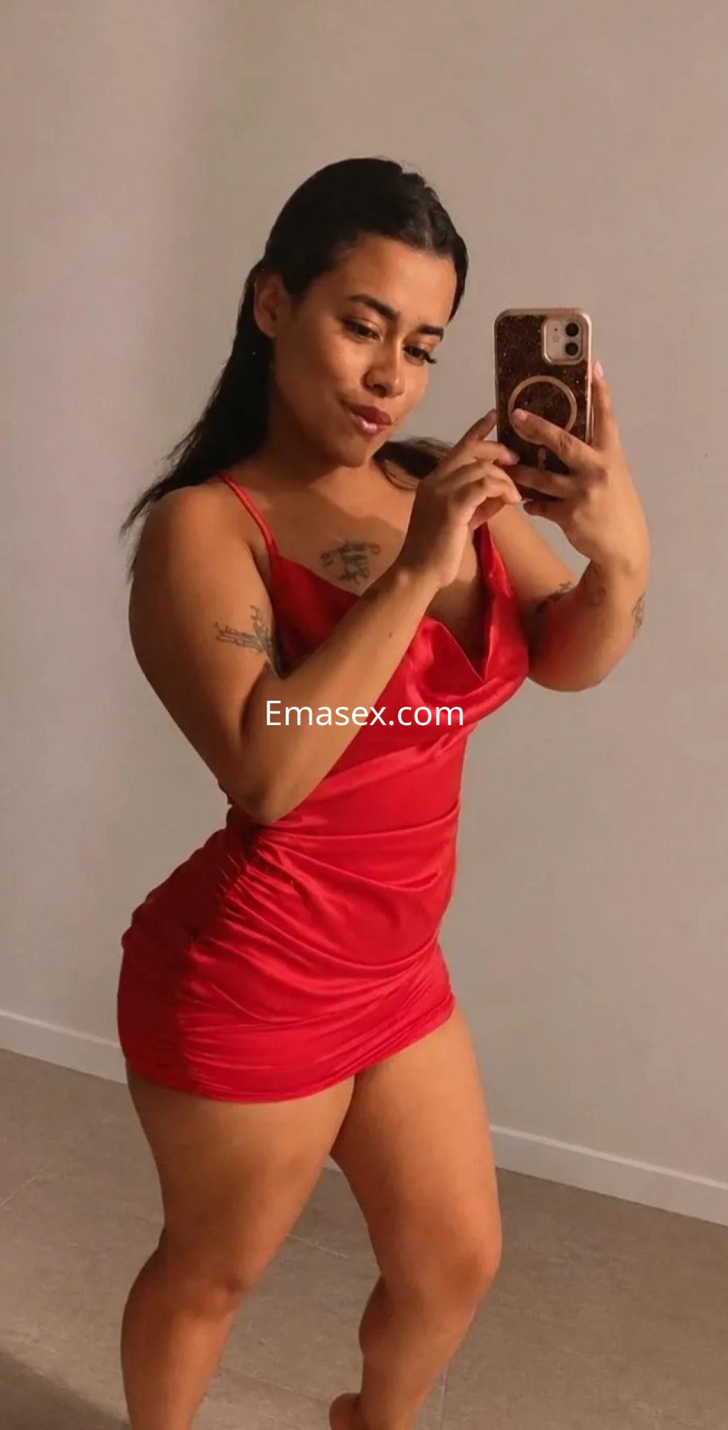 Escort en Valencia con vestido rojo ajustado, posando frente a un espejo, mostrando una expresión coqueta.