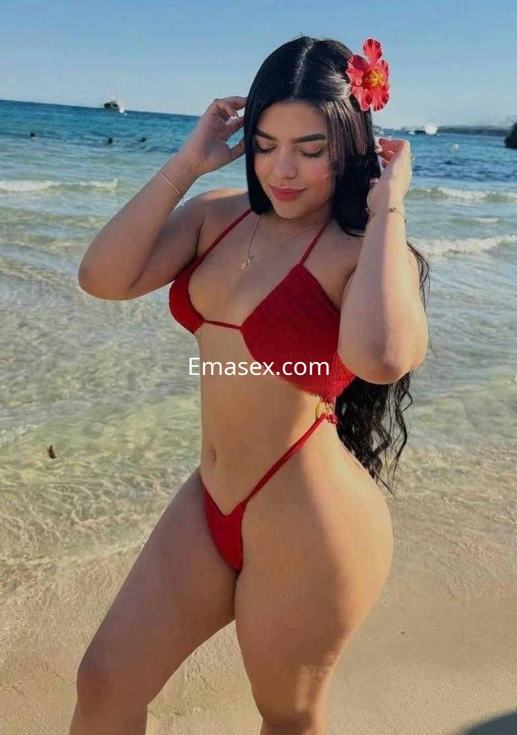 Puta posando en la playa de Valladolid, con un bikini rojo y un toque de flor en el cabello.