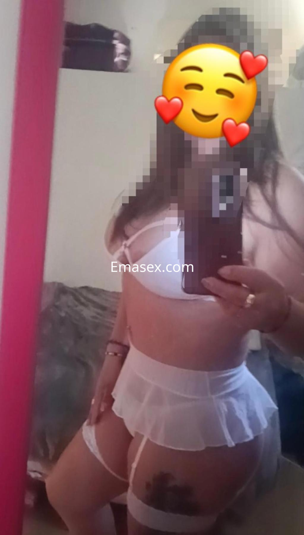 Escort en Vitoria, posando frente al espejo con lencería blanca y una falda corta, mostrando su figura.