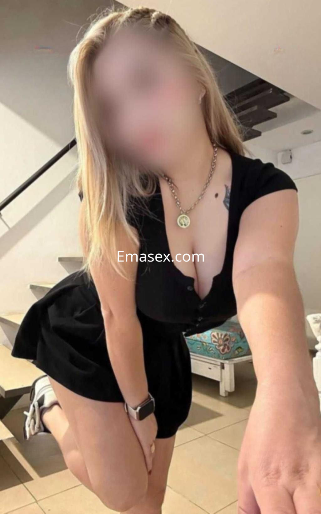 Escort en Valladolid con cabello rubio, vestido negro ajustado y pose coqueta en un ambiente interior.
