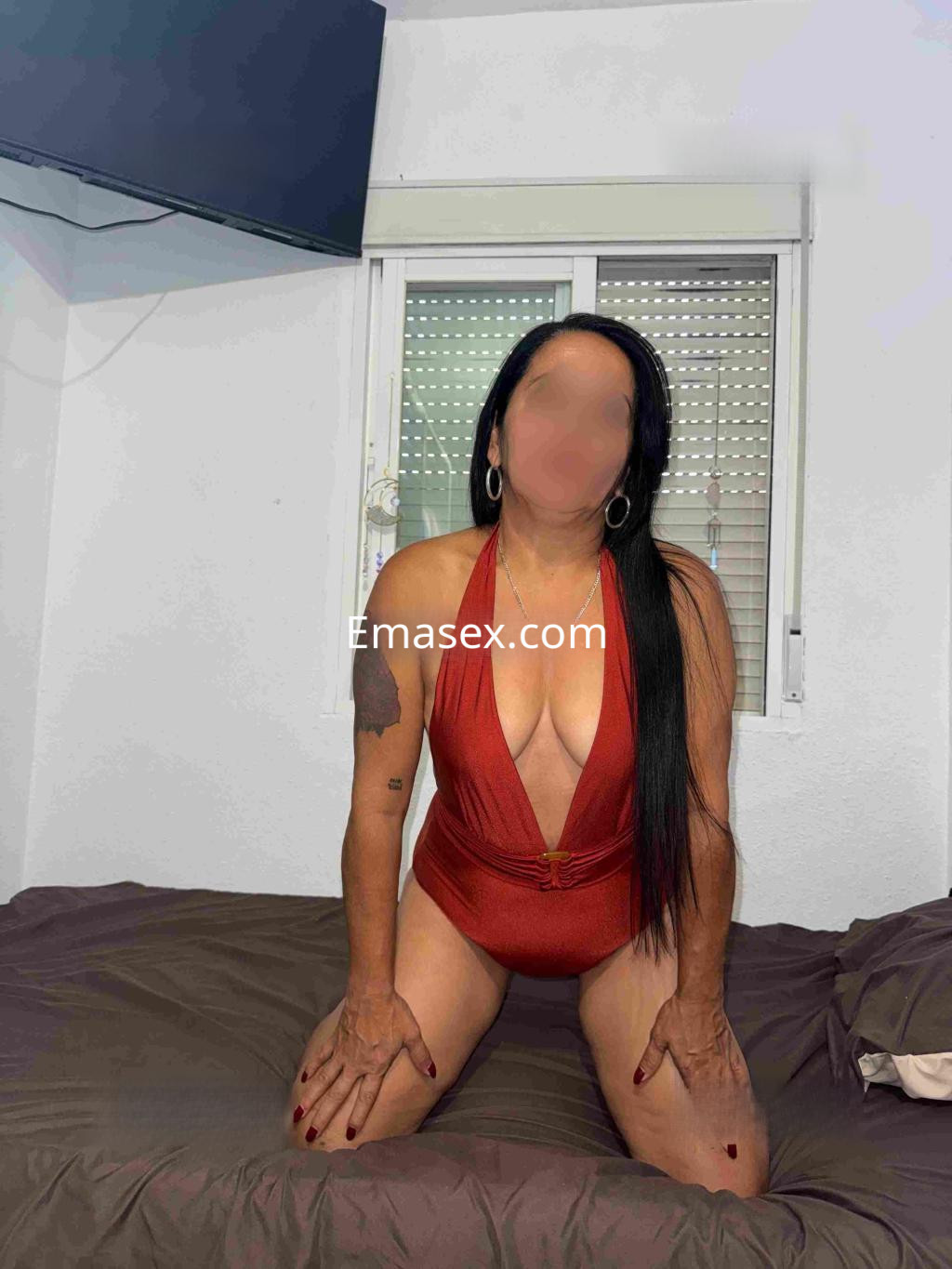 Puta en Cáceres, con cabello largo y lacio, usa un traje de baño rojo mientras se encuentra sentada en una cama.