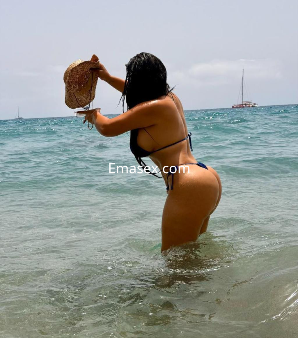 La puta está en el agua en Tenerife, usando un bikini azul y sosteniendo un sombrero mientras se agacha.