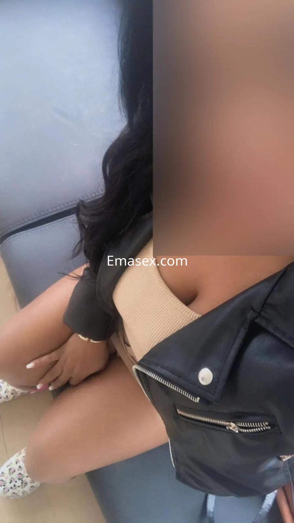 Escort en Valladolid con cabello largo y oscuro, vistiendo un top claro y chaqueta negra, sentada en un sofá.