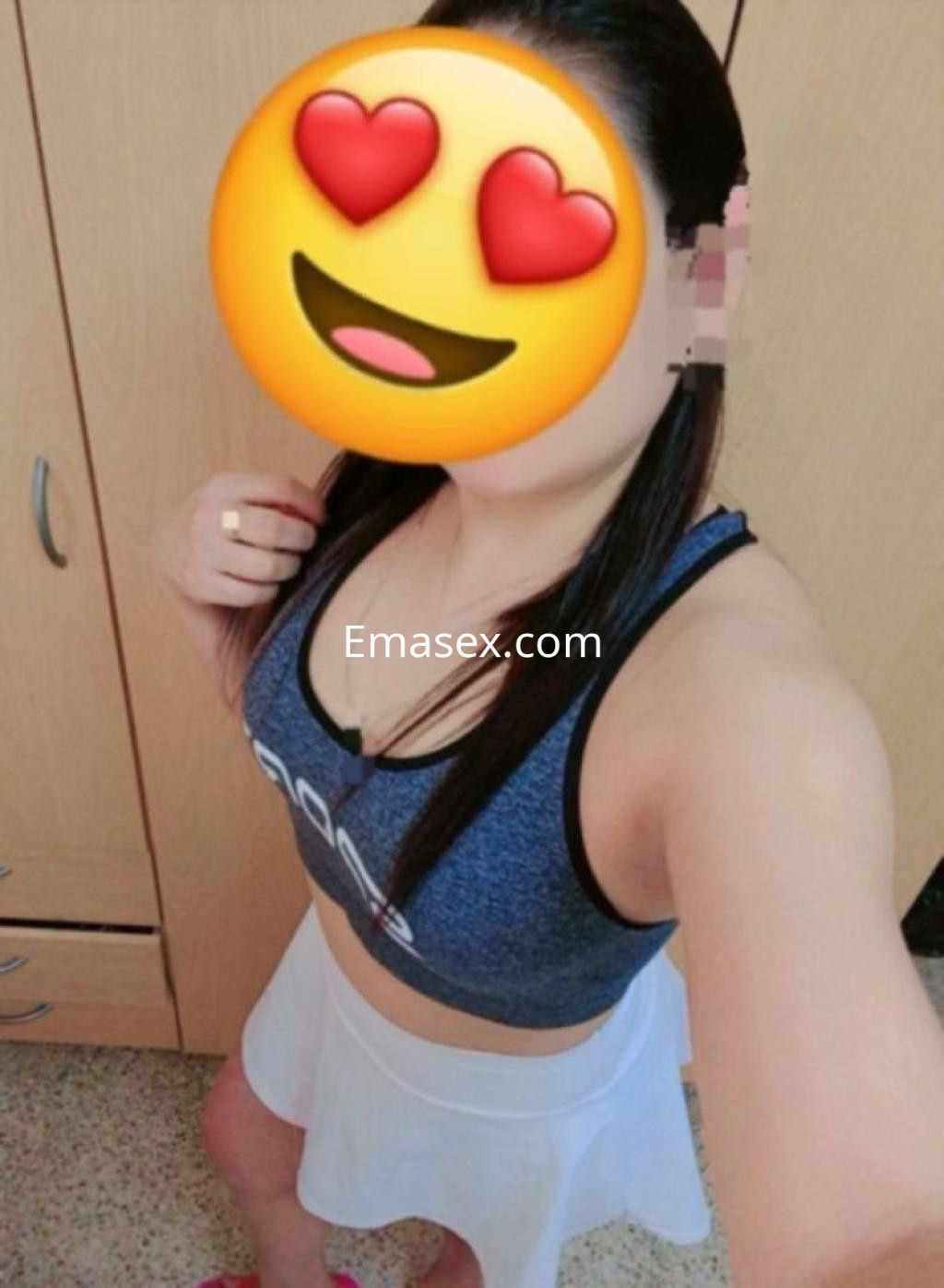 Escort en Zaragoza posando de lado, vistiendo una blusa deportiva y una falda blanca, con cabello largo.