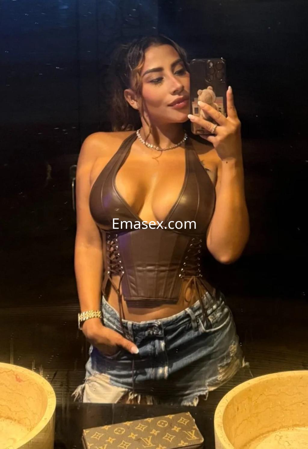 Escort en Málaga posando frente a un espejo, con blusa ajustada y jeans cortos, mostrando confianza.
