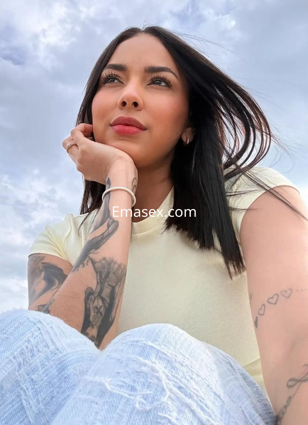 Escort en Málaga con cabello oscuro y lacio, usando una camiseta amarilla y jeans, posando al aire libre.
