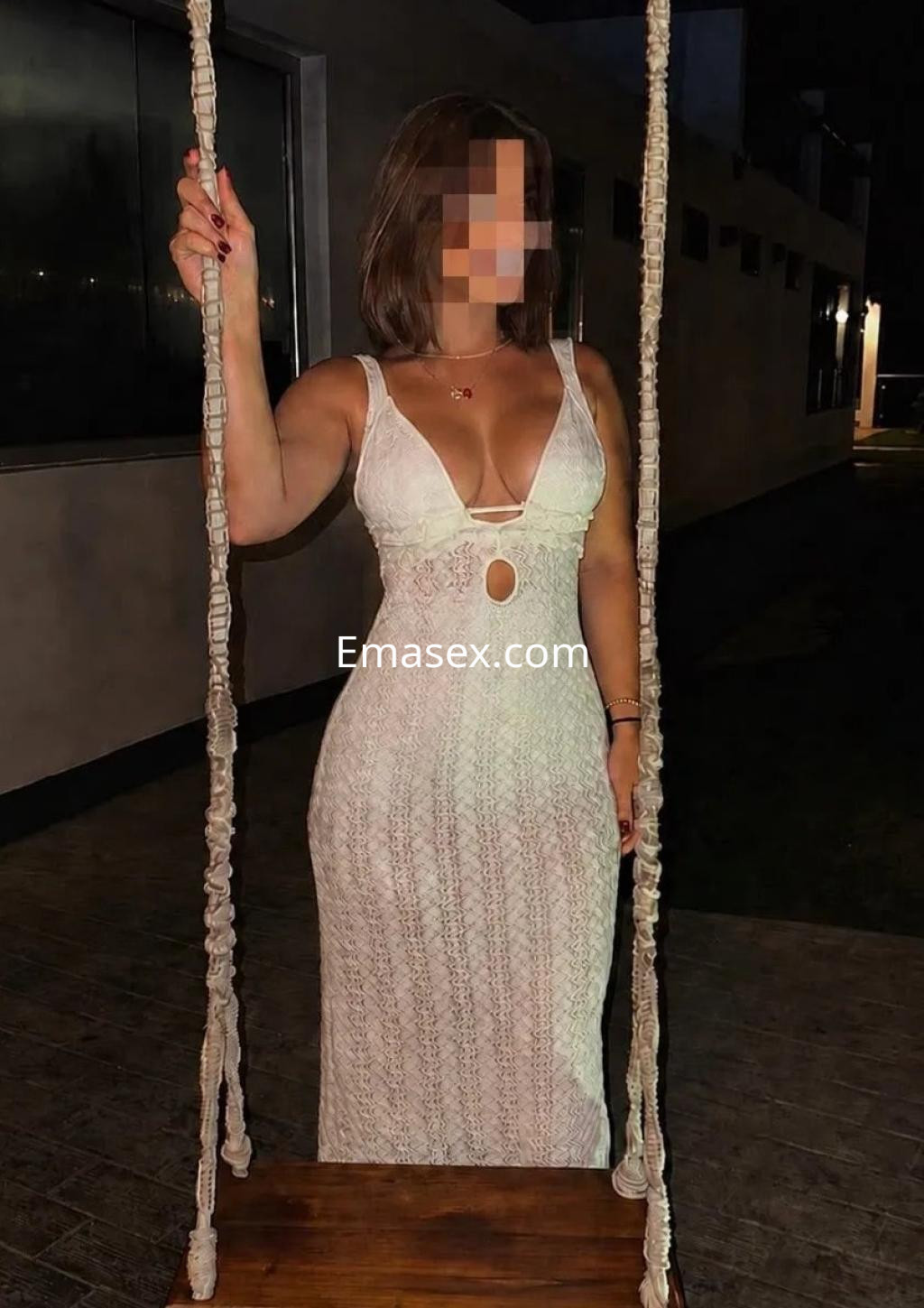 Puta con vestido blanco de encaje, posando en un columpio al aire libre en Málaga, con un fondo iluminado.