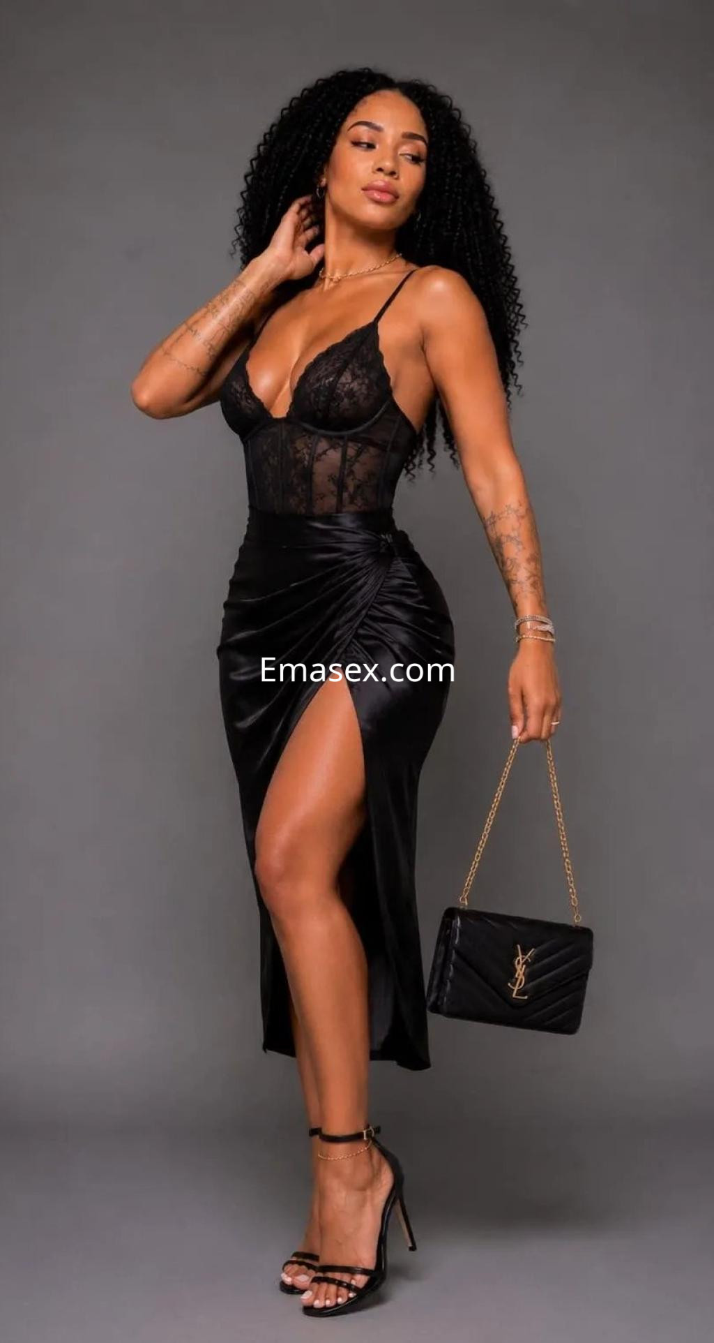 Escort en Palma de Mallorca, vistiendo un vestido negro con transparencias y una abertura, sosteniendo un bolso.