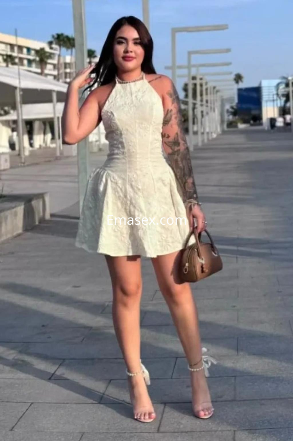 Escort en Alicante con vestido blanco ajustado y sin mangas, mostrando un tatuaje en su brazo izquierdo.