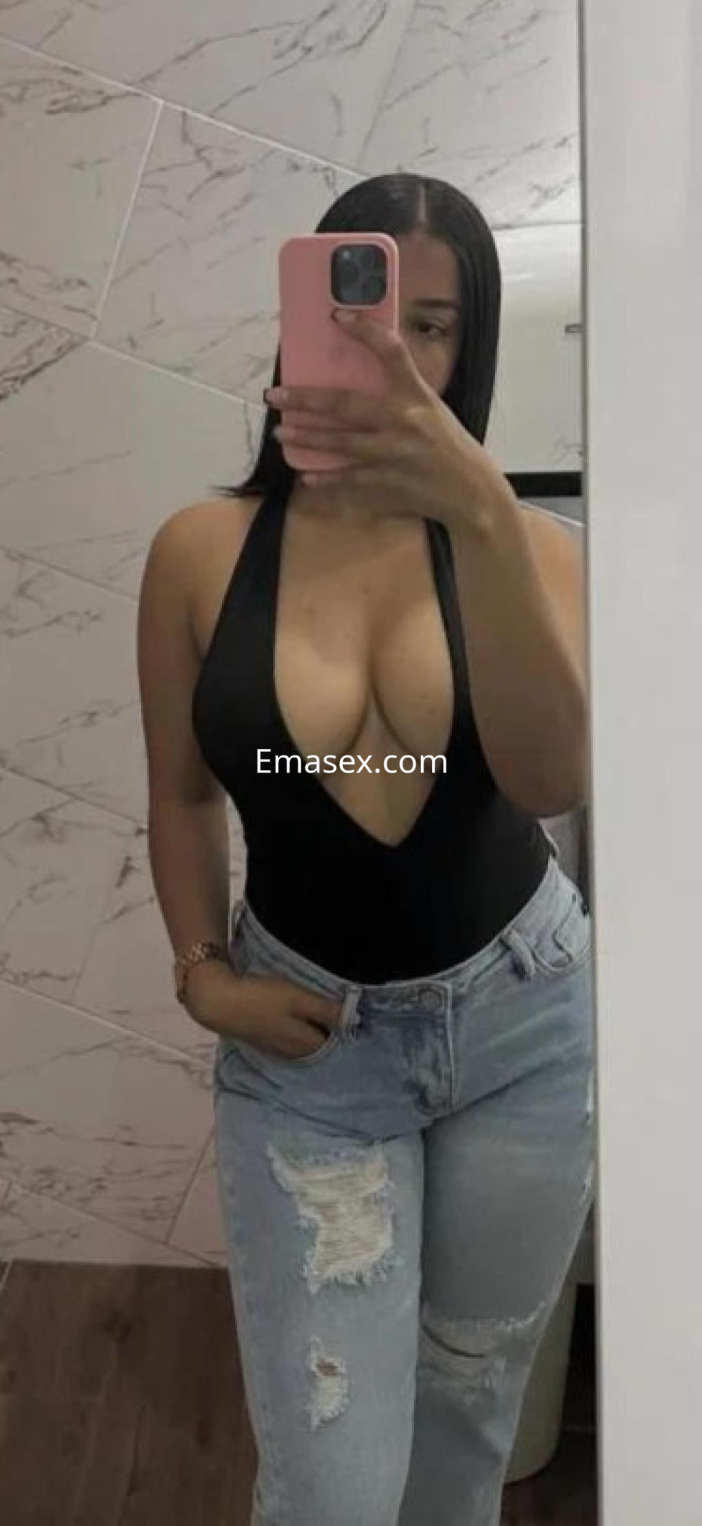 Puta en Tarragona luce un body negro profundo y jeans desgastados, posando frente a un espejo.