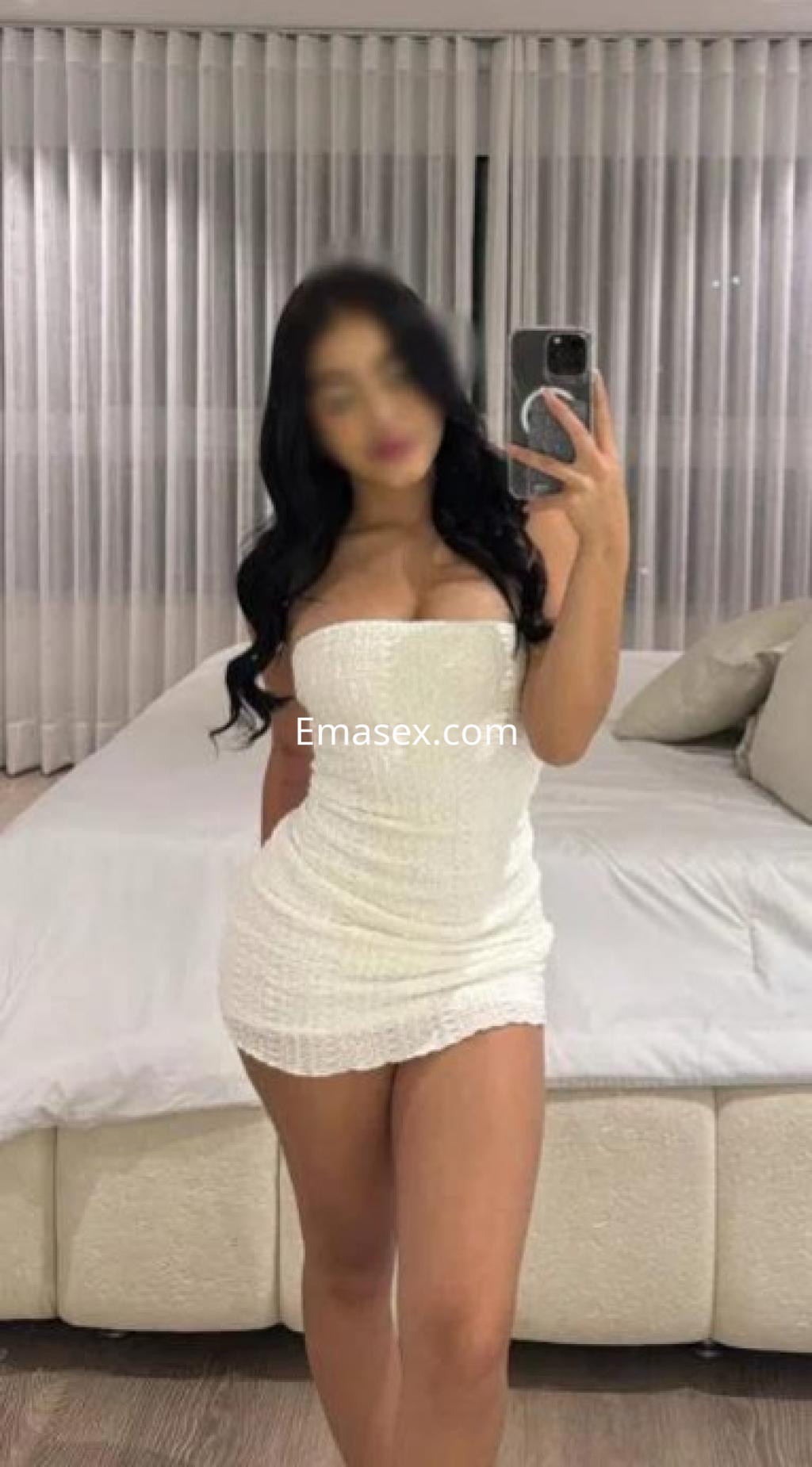 Escort en Badajoz con cabello negro, luciendo un vestido blanco ajustado mientras se toma una selfie frente a un espejo.