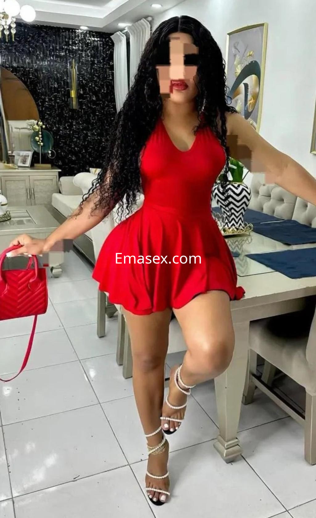 Puta posando en un vestido rojo ajustado, con cabello rizado y una bolsa roja, en un elegante interior de Valladolid.