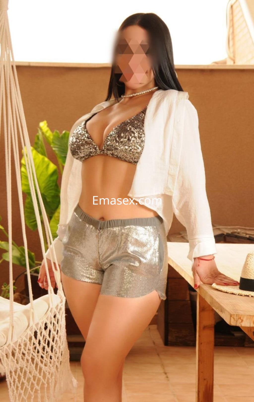 Puta en Valladolid, luciendo un top brillante y shorts plateados, posando en un ambiente iluminado y relajado.