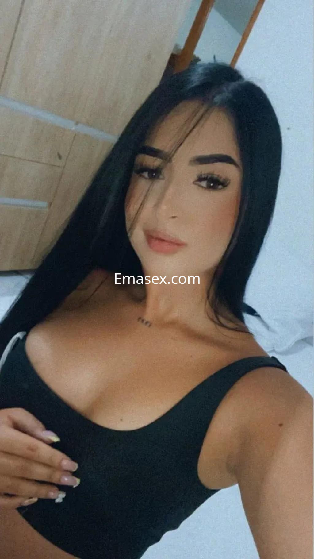 Escort con cabello largo y lacio, viste una blusa negra ajustada, sonriendo en un ambiente luminoso en Vigo.