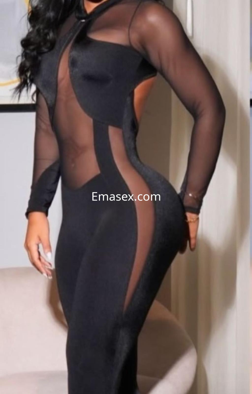 Escort en Tarragona viste un elegante body negro ajustado con detalles transparentes, posando de lado.