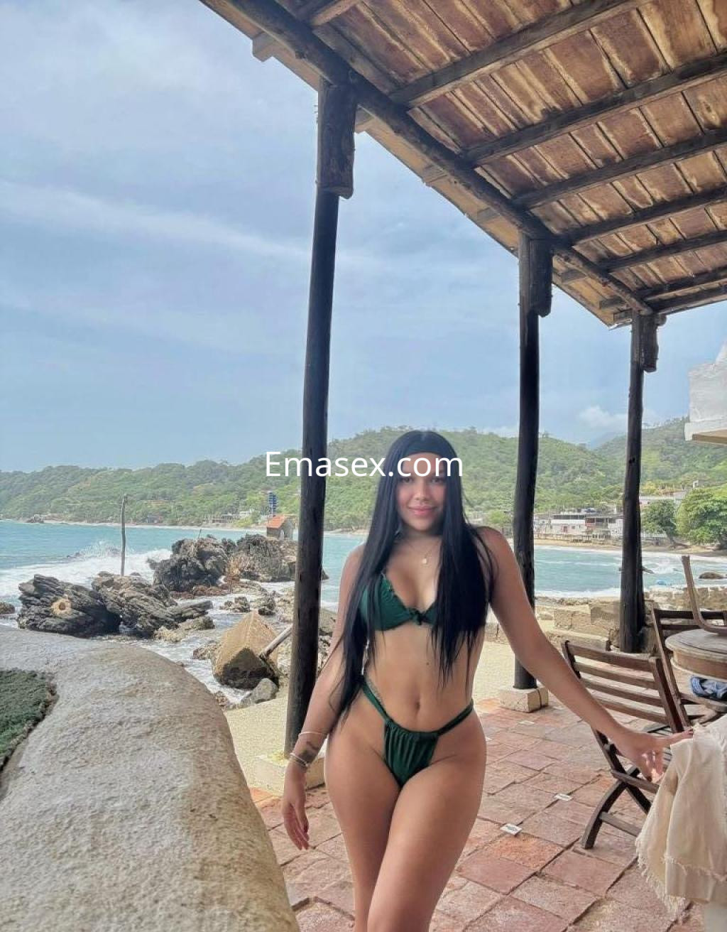Puta en Tarragona luciendo un bikini verde, posando con el mar y un paisaje tropical de fondo.
