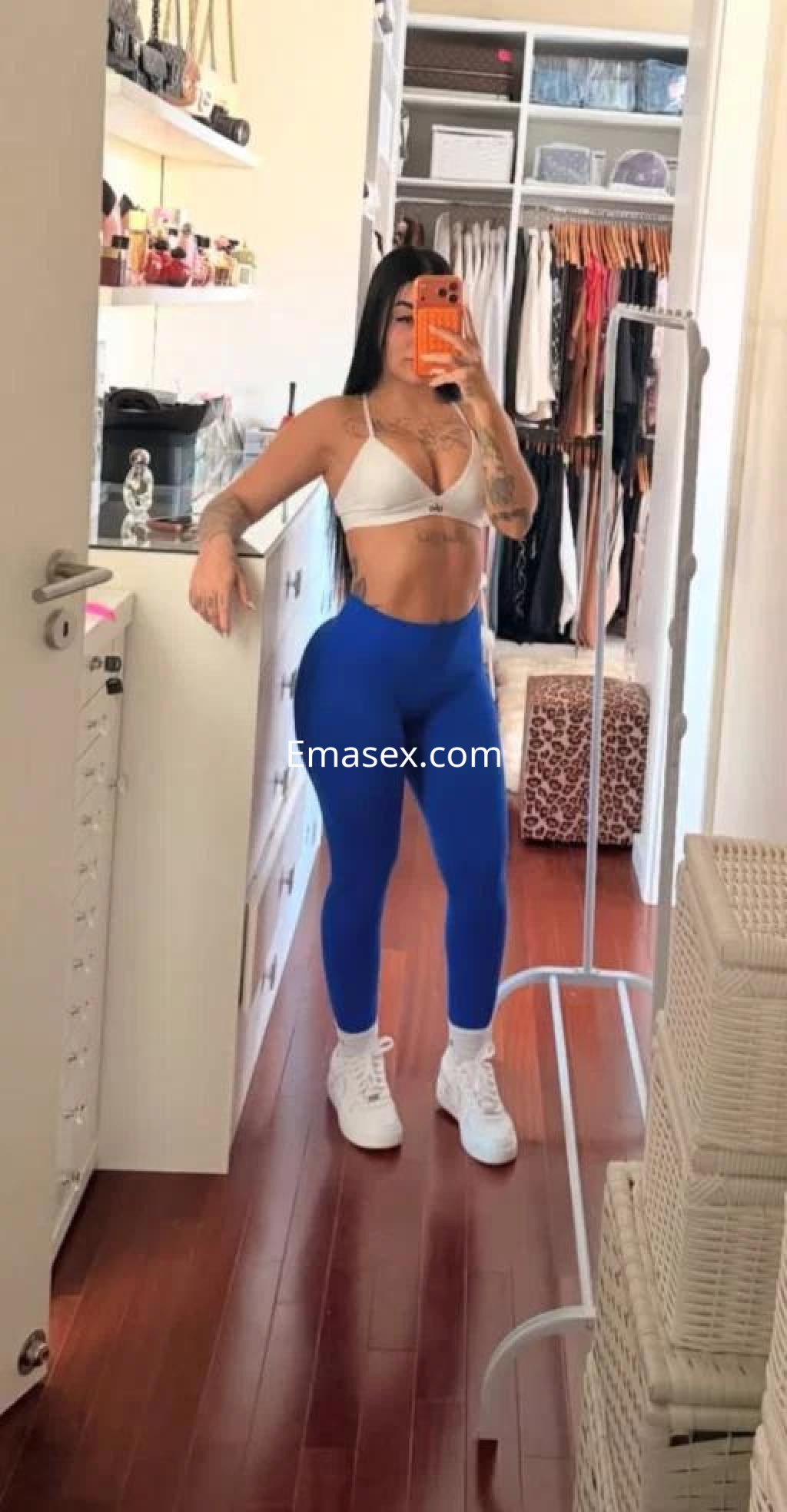 Puta en Tarragona posando en un espejo, con un top blanco y leggings azules, mostrando su figura atlética.