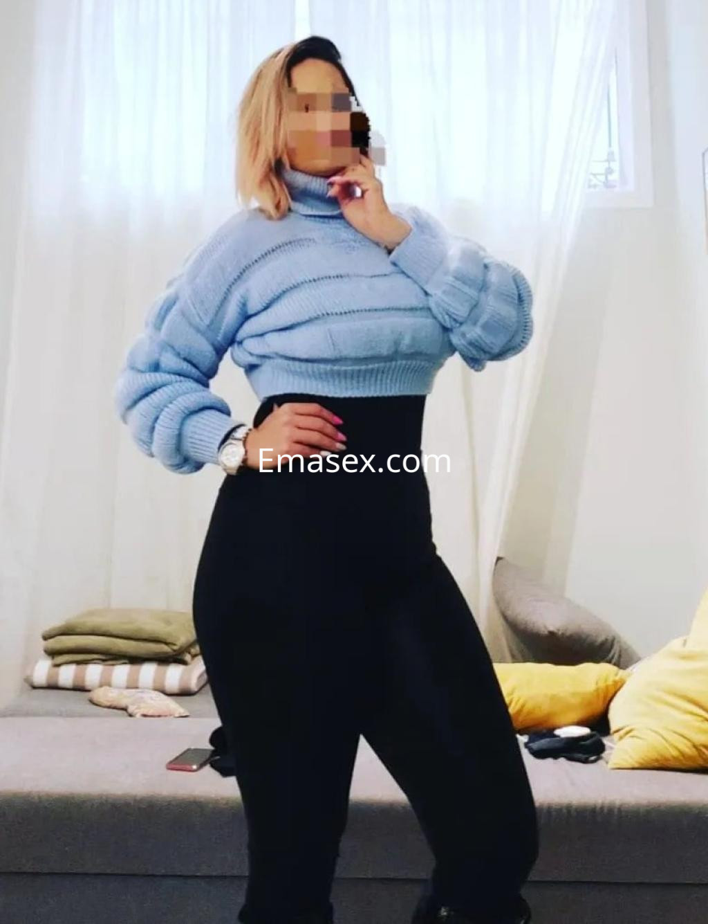 Escort de Cádiz posando con un suéter azul claro y pantalones ajustados en un ambiente acogedor.