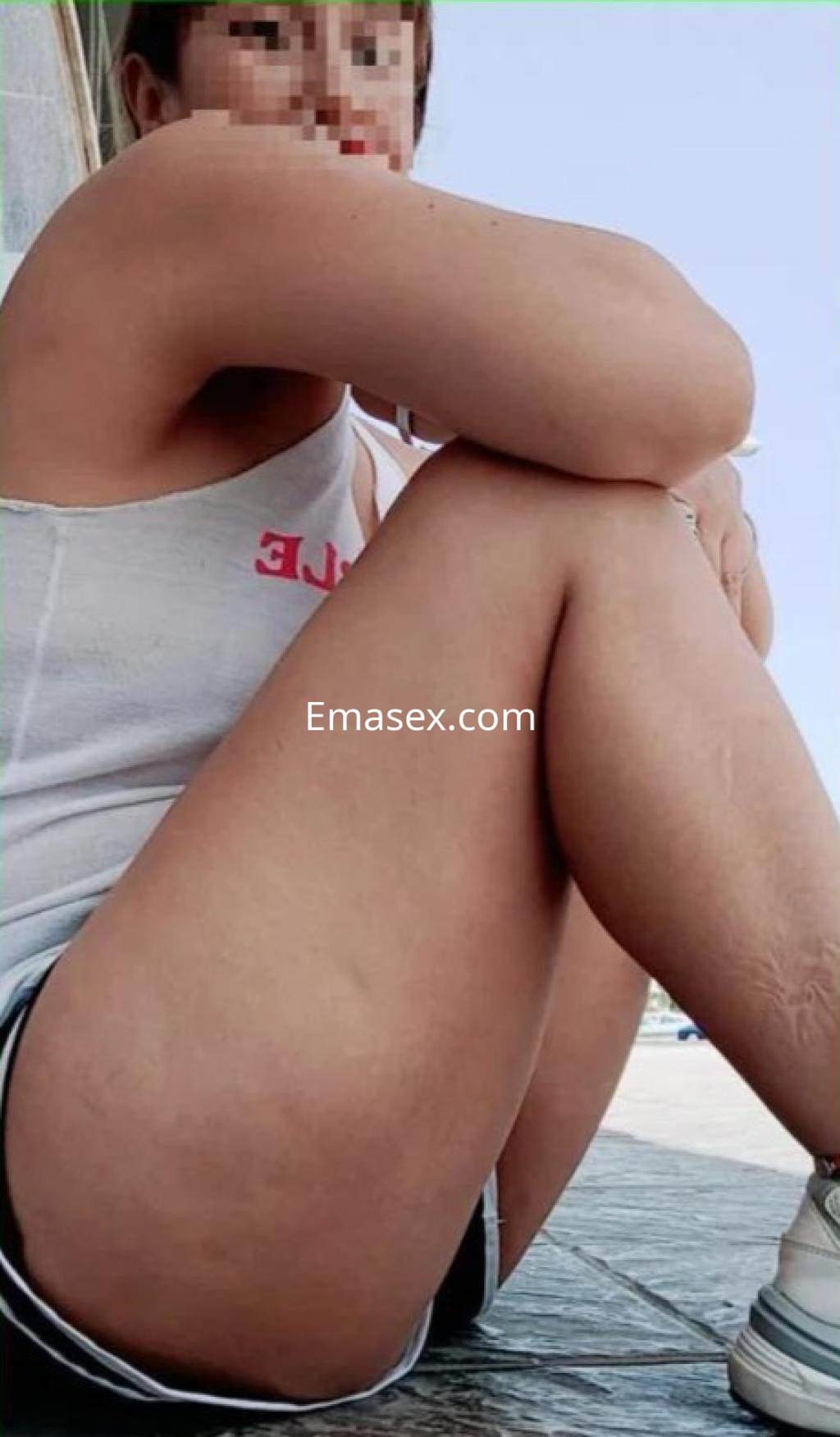 Escort en Cádiz, sentada con las piernas cruzadas, viste una camiseta sin mangas y pantalones cortos.