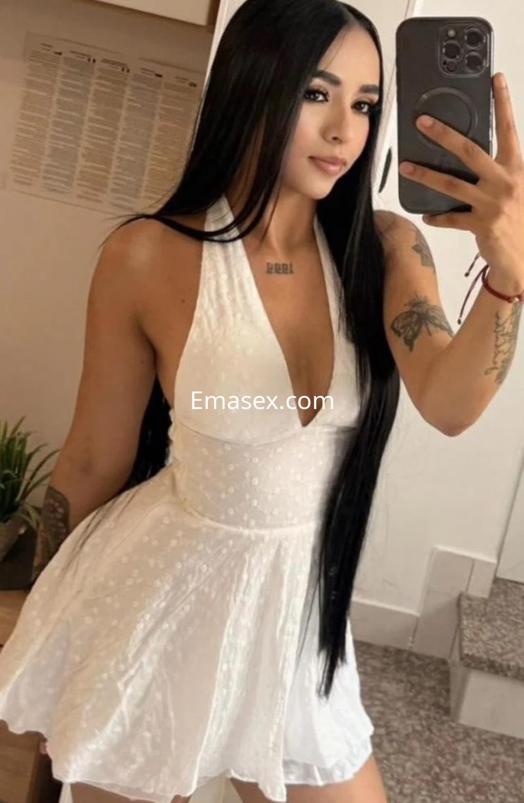 Escort en Cádiz con vestido blanco sin mangas, cabello largo y lacio, mostrando una pose sonriente en un ambiente interior.