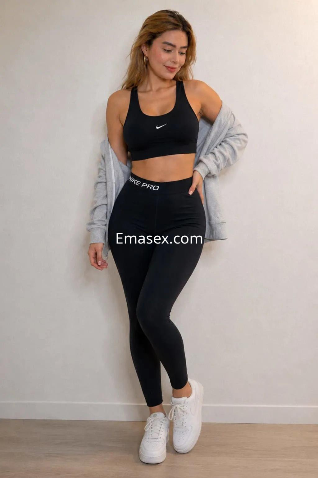 Escort en Alicante luciendo un conjunto deportivo negro, con top y leggins, y una chaqueta gris, sonriendo.