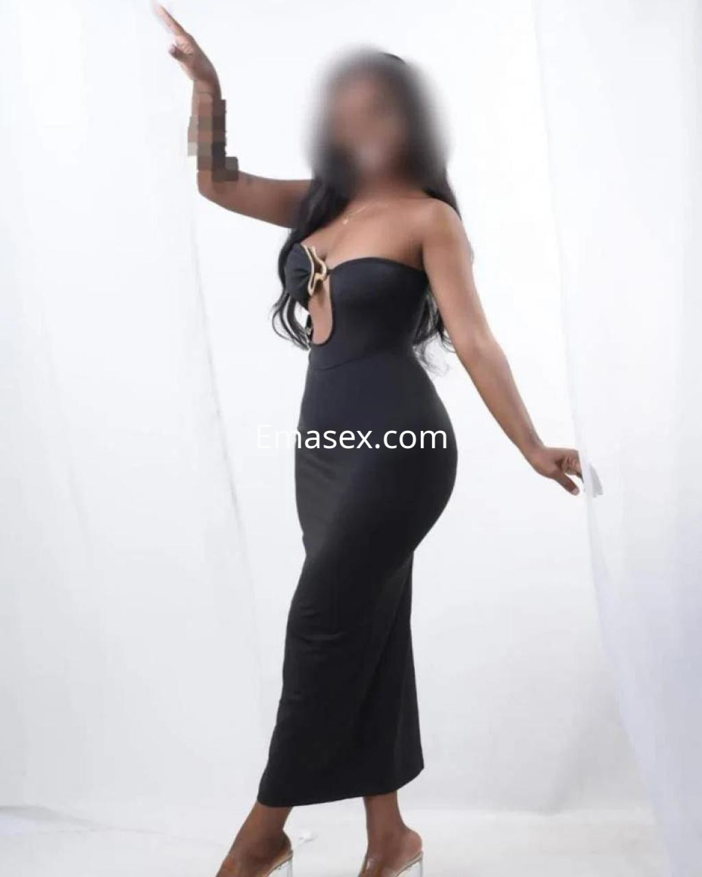 Puta en Girona luciendo un vestido negro ajustado con un escote pronunciado y sandalias transparentes.