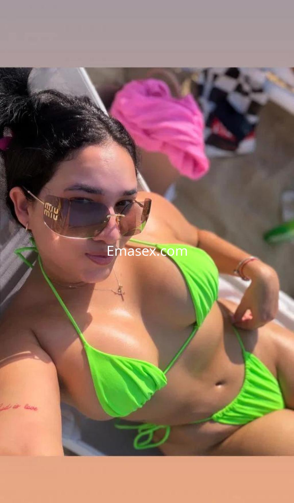 Escort en Huelva, luciendo un bikini verde brillante y gafas de sol, posando en un ambiente de playa.