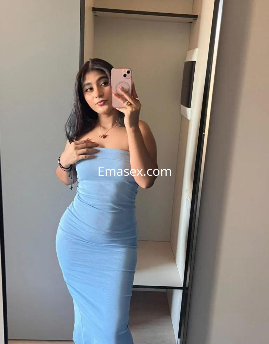Escort en Madrid posando frente a un espejo, luciendo un vestido azul ceñido y con cabello largo y oscuro.