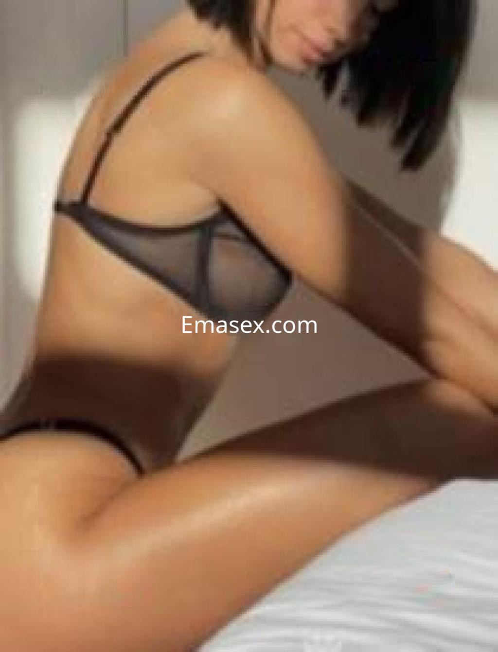 Escort en Salamanca posando de perfil, luciendo lencería negra y con el cabello corto, sentada sobre una cama.